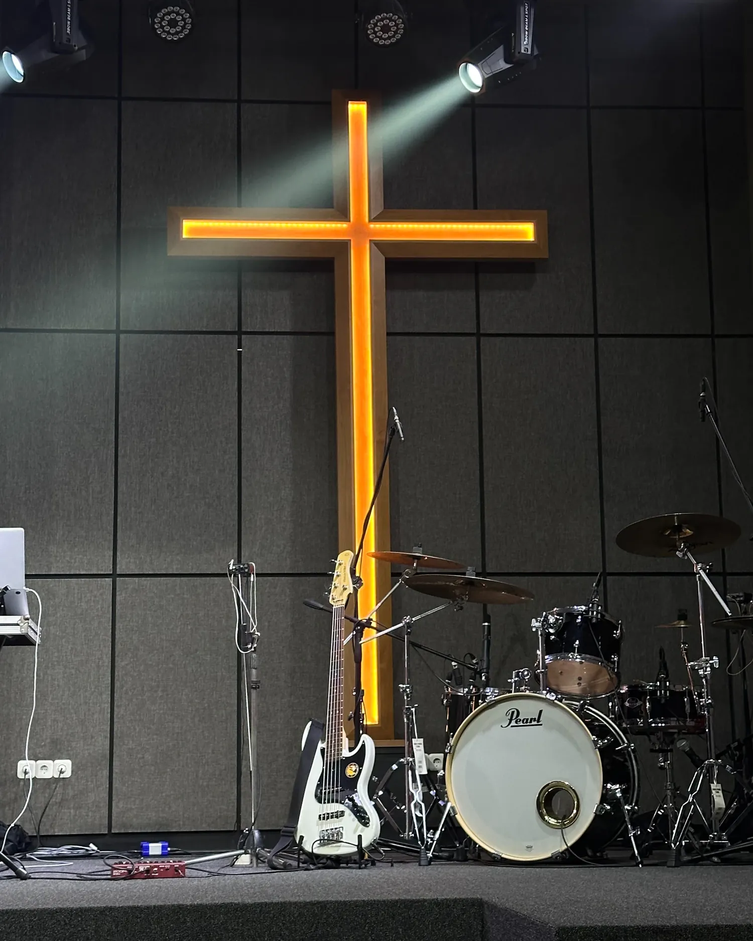 A worship keyboardist leading from a darkened stage as light falls on a cross.